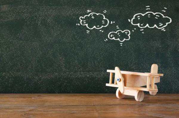 Image of old wooden airplane toy on wooden table in front of set of infographics over textured chalkboard. — Stock Photo, Image