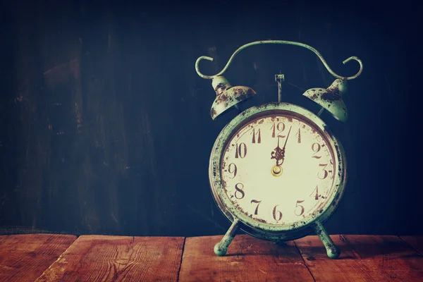 Vintage filtered image of old alarm clock on wooden table in front of black wooden background. — Stockfoto