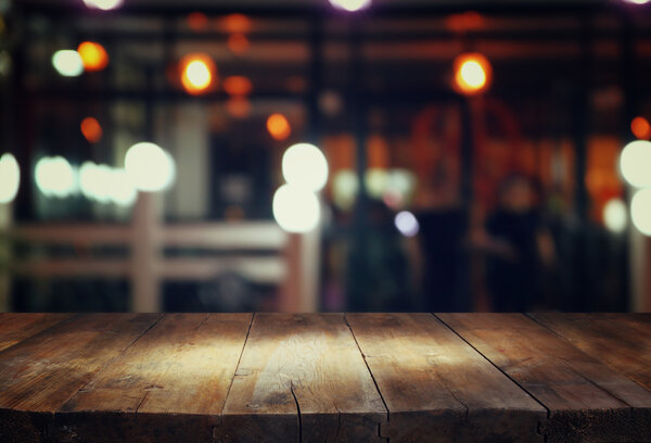 image of wooden table in front of abstract blurred background of resturant lights.