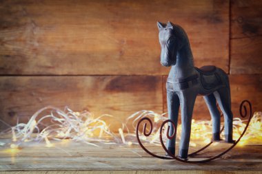 image of rocking horse and magic christmas lights on wooden table. retro filtered image.