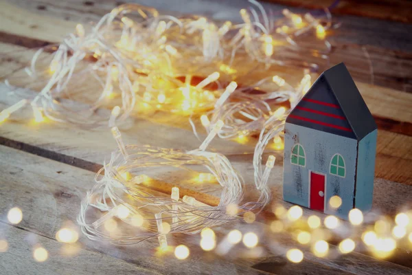 Dekoratives Haus neben goldenen Girlanden Lichter auf Holzgrund. Kopierraum. — Stockfoto