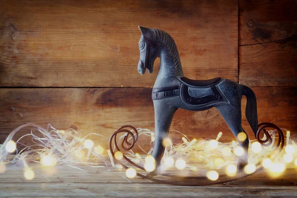 Imagem do cavalo de balanço e luzes mágicas do Natal na mesa de madeira. imagem retro filtrada . — Fotografia de Stock