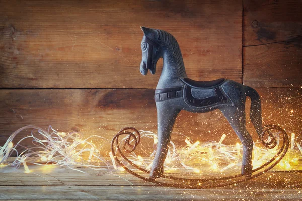 Image of rocking horse and magic christmas lights on wooden table. retro filtered image. — Stock Fotó
