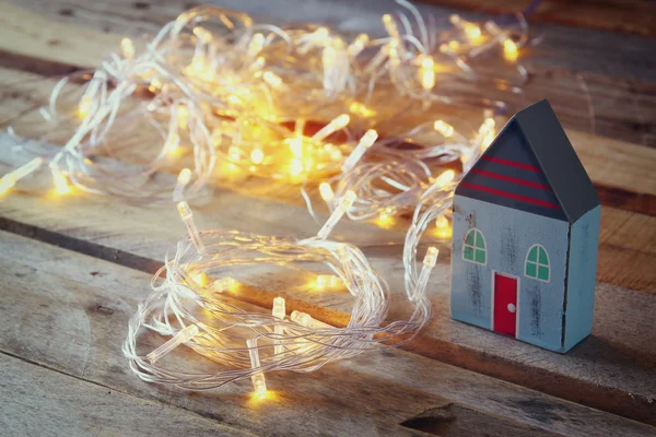 Dekoratives Haus neben goldenen Girlanden Lichter auf Holzgrund. Kopierraum. — Stockfoto