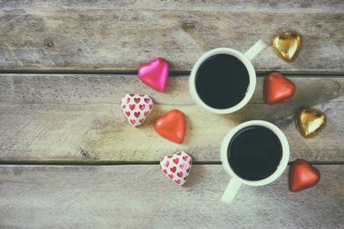 top view image of colorful heart shape chocolates and couple mugs of coffee  on wooden table. valentine's day celebration concept.