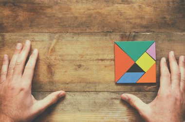 kayıp bir parça kare tangram bulmacanın içinde ahşap masa üzerinde tutan adamın el fotoğrafı Üstten Görünüm