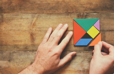 kayıp bir parça kare tangram bulmacanın içinde ahşap masa üzerinde tutan adamın el fotoğrafı Üstten Görünüm
