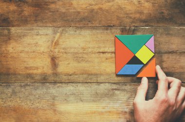 kayıp bir parça kare tangram bulmacanın içinde ahşap masa üzerinde tutan adamın el fotoğrafı Üstten Görünüm