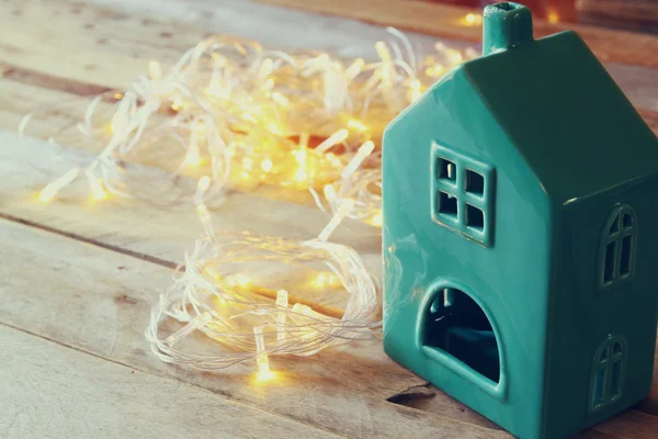 Foto de la casa decorativa junto a luces de guirnalda de oro sobre fondo de madera. espacio de copia. retro filtrado . —  Fotos de Stock