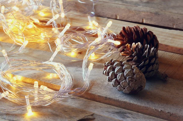 Conos de pino junto a luces de guirnalda de oro sobre fondo de madera. espacio de copia . — Foto de Stock