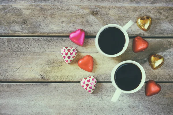 Imagem vista superior de chocolates forma de coração colorido e canecas par de café na mesa de madeira. Conceito de celebração do dia dos namorados . — Fotografia de Stock