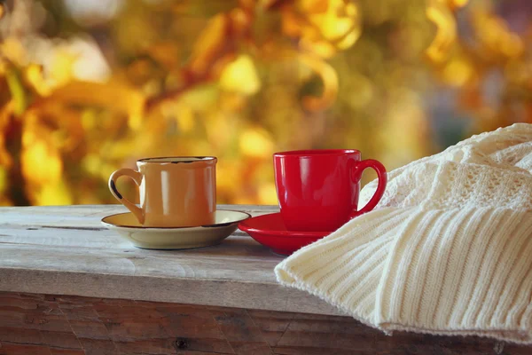 Front image of two coffee cups over wooden table and woolen sweater in front of autumnal sunset background. Valentines Day concept. — Stock Photo, Image