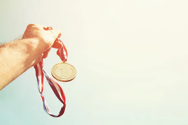 Mann hob die Hand und hielt Goldmedaille gegen den Himmel. Auszeichnung und Siegerkonzept. Selektiver Fokus. Bild im Retro-Stil — Stockfoto