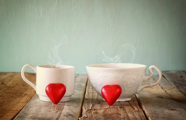 Image of tow red heart shape chocolates and couple cups of coffee on wooden table. valentine's day celebration concept. vintage filtered. — Stock Photo, Image