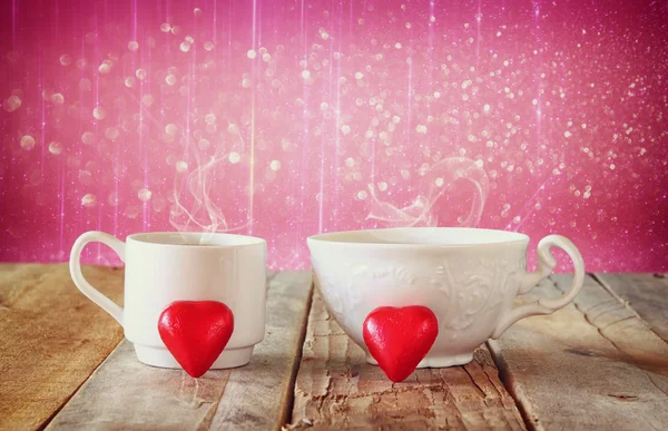 Imagen de remolcar bombones en forma de corazón rojo y un par de tazas de café en la mesa de madera frente al fondo abstracto bokeh. concepto de celebración del día de San Valentín . — Foto de Stock