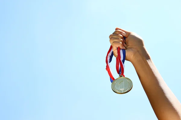 Woman hand raised, holding gold medal against sky. award and victory concept. — Stock Photo, Image