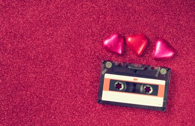 top view image of colorful heart shape chocolates and audio cassette on red glitter background. valentine's day celebration concept.