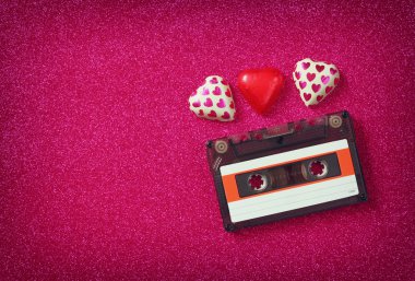 top view image of colorful heart shape chocolates and audio cassette on red glitter background. valentine's day celebration concept.
