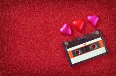 top view image of colorful heart shape chocolates and audio cassette on red glitter background. valentine's day celebration concept.