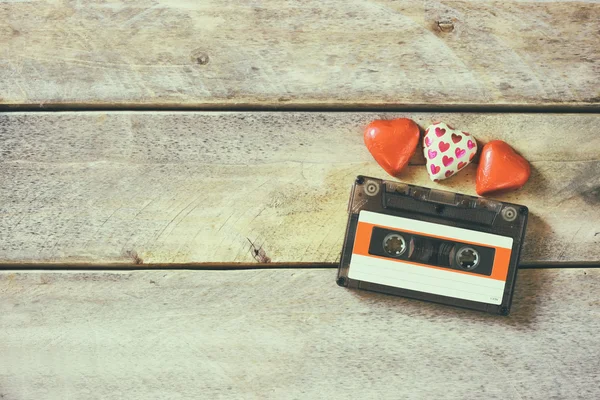 Top view image of colorful heart shape chocolates and audio cassette on wooden table. valentine's day celebration concept. retro toned and filtered. — Stockfoto