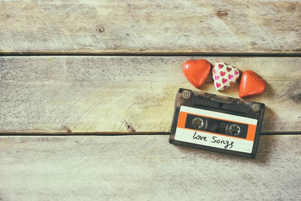 Top view image of colorful heart shape chocolates and audio cassette on wooden table. valentine's day celebration concept. retro toned and filtered. — Stockfoto