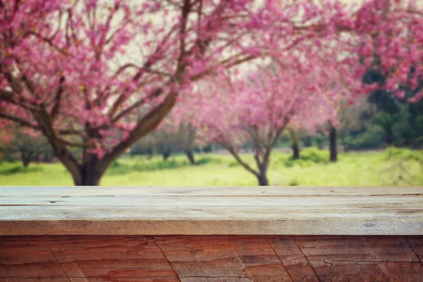 Деревянный деревенский стол перед весенним цветущим сакурой. Ретро фильтрованное изображение. демонстрация продукции и концепция пикника . — стоковое фото