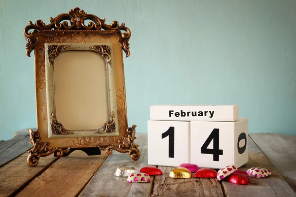 14 de febrero calendario vintage de madera con coloridos chocolates en forma de corazón junto al marco vintage en blanco en la mesa de madera. enfoque selectivo.Plantilla listo para poner la fotografía —  Fotos de Stock