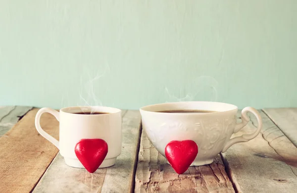 Image of two red heart shape chocolates and couple cups of coffee on wooden table. valentine's day celebration concept. vintage filtered. — Stock Photo, Image