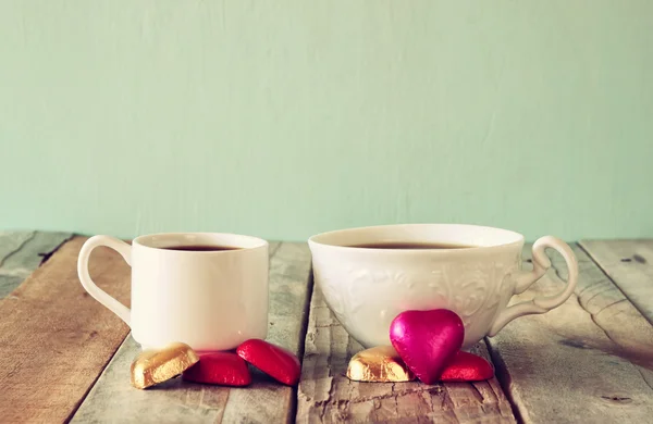 图像的两个红色的心形状巧克力和几杯咖啡木制的桌子上。情人节那天庆祝概念。老式过滤. — 图库照片