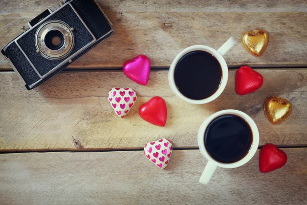 Top view image of colorful heart shape chocolates, fabric heart, vintage photo camera and cup of coffee on wooden table. valentine's day celebration concept — 图库照片
