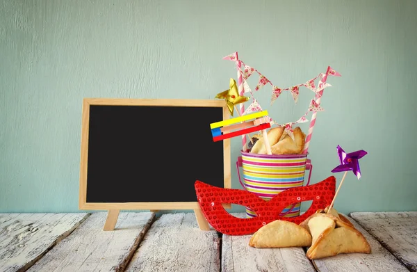 Hamantaschen biscuits ou hamans oreilles, bruyant et masque à côté du tableau noir pour la célébration de Pourim (fête du carnaval juif). focus sélectif — Photo