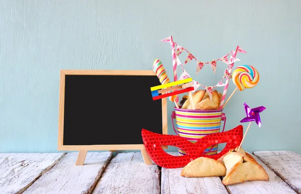 Hamantaschen cookies or hamans ears,noisemaker and mask next to blackboard for Purim celebration (jewish carnival holiday). selective focus — Stockfoto