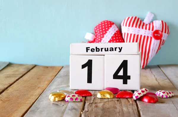 14 лютого дерев'яний старовинний календар з різнокольоровими шоколадними цукерками у формі серця на дерев'яному столі. вибірковий фокус. вінтажний фільтр — стокове фото