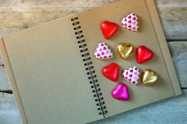 top view image of colorful heart shape chocolates on open blank notebook on wooden table. valentine's day celebration concept. retro filtered ans toned image