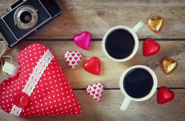 Top view image of colorful heart shape chocolates, fabric heart, vintage photo camera and cup of coffee on wooden table. valentine's day celebration concept — ストック写真