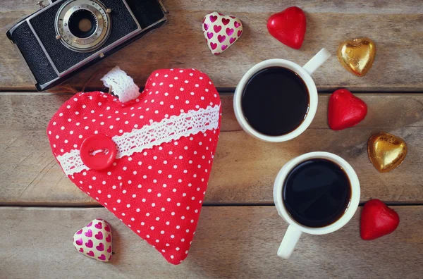 Imagem vista superior de chocolates forma de coração colorido, coração de tecido, câmera de foto vintage e xícara de café na mesa de madeira. Conceito de celebração do dia dos namorados — Fotografia de Stock