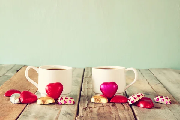 Image of two red heart shape chocolates and couple cups of coffee on wooden table. valentine's day celebration concept. vintage filtered — Stock Photo, Image