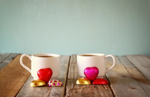 Image of two red heart shape chocolates and couple cups of coffee on wooden table. valentine's day celebration concept. vintage filtered — Stock Photo, Image