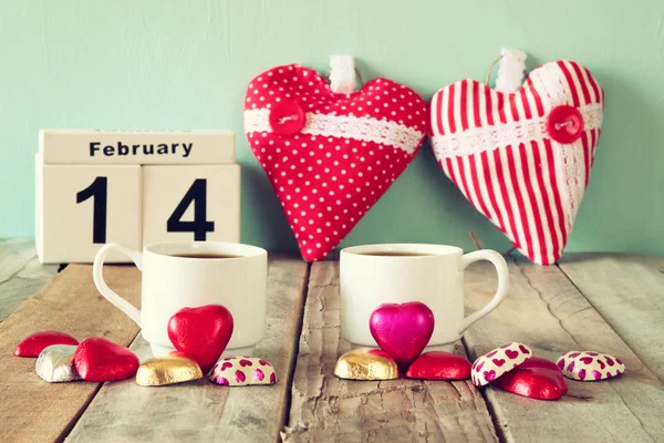 14 février calendrier vintage en bois avec des chocolats colorés en forme de coeur à côté de deux tasses sur une table en bois. focalisation sélective. vintage filtré — Photo