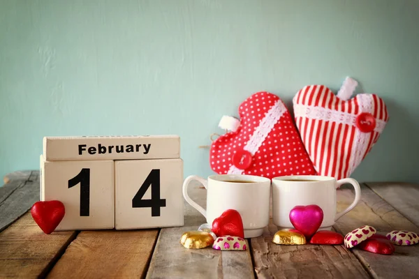 14 février calendrier vintage en bois avec des chocolats colorés en forme de coeur à côté de deux tasses sur une table en bois. focalisation sélective. vintage filtré — Photo