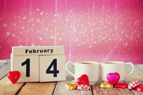 February 14th wooden vintage calendar with colorful heart shape chocolates next to couple cups on wooden table. selective focus. vintage filtered — Stock Photo, Image