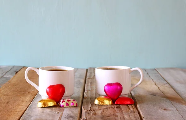 Εικόνα της ρυμούλκησης κόκκινη καρδιά σχήμα σοκολάτες και δύο φλιτζάνια καφέ σε ξύλινο τραπέζι. ημέρα του Αγίου Βαλεντίνου γιορτή έννοια. τρύγου φιλτραρισμένη — Φωτογραφία Αρχείου