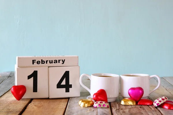 14 de febrero calendario vintage de madera con coloridos chocolates en forma de corazón junto a un par de copas en la mesa de madera. enfoque selectivo. filtrado vintage —  Fotos de Stock
