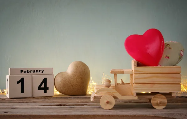 Foto del 14 de febrero calendario vintage de madera con camión de juguete de madera con corazones delante de pizarra. Concepto de celebración del día de San Valentín. filtrado vintage —  Fotos de Stock