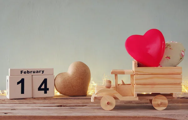 Фотографія 14 лютого дерев'яного старовинного календаря з дерев'яною іграшковою вантажівкою з сердечками перед дошкою. Концепція святкування Дня Святого Валентина. вінтажний фільтр — стокове фото
