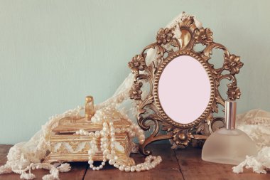 Antique blank victorian style frame, perfume bottle and white pearls on wooden table. template, ready to put photography