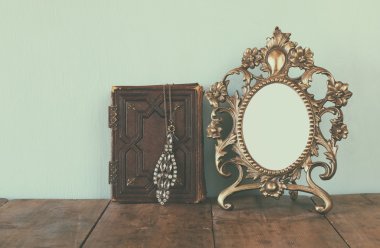 Antique blank victorian style frame and old book with vintage necklace on wooden table. retro filtered image. template, ready to put photography