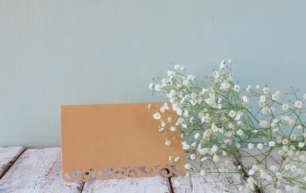 fresh white flowers next to vintage empty card over wooden table. vintage filtered and toned image