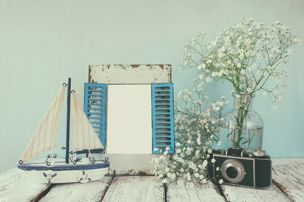 Стара старовинна дерев'яна рамка, білі квіти, фотоапарат і вітрильний човен на дерев'яному столі. вінтажне фільтроване зображення. концепція морського способу життя. шаблон, готовий поставити фотографію — стокове фото