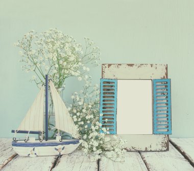 old vintage wooden frame, white flowers and sailing boat on wooden table. vintage filtered and toned image. nautical lifestyle concept. template, ready to put photography